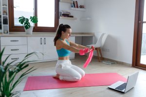 jeune fille assisse sur un tapis de sport roose qui fait du spott en ligne devant son ordinateur